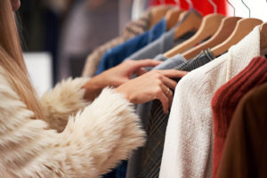 Woman in a cream-colored fur coat shopping through women’s boutique clothing on wooden hangers